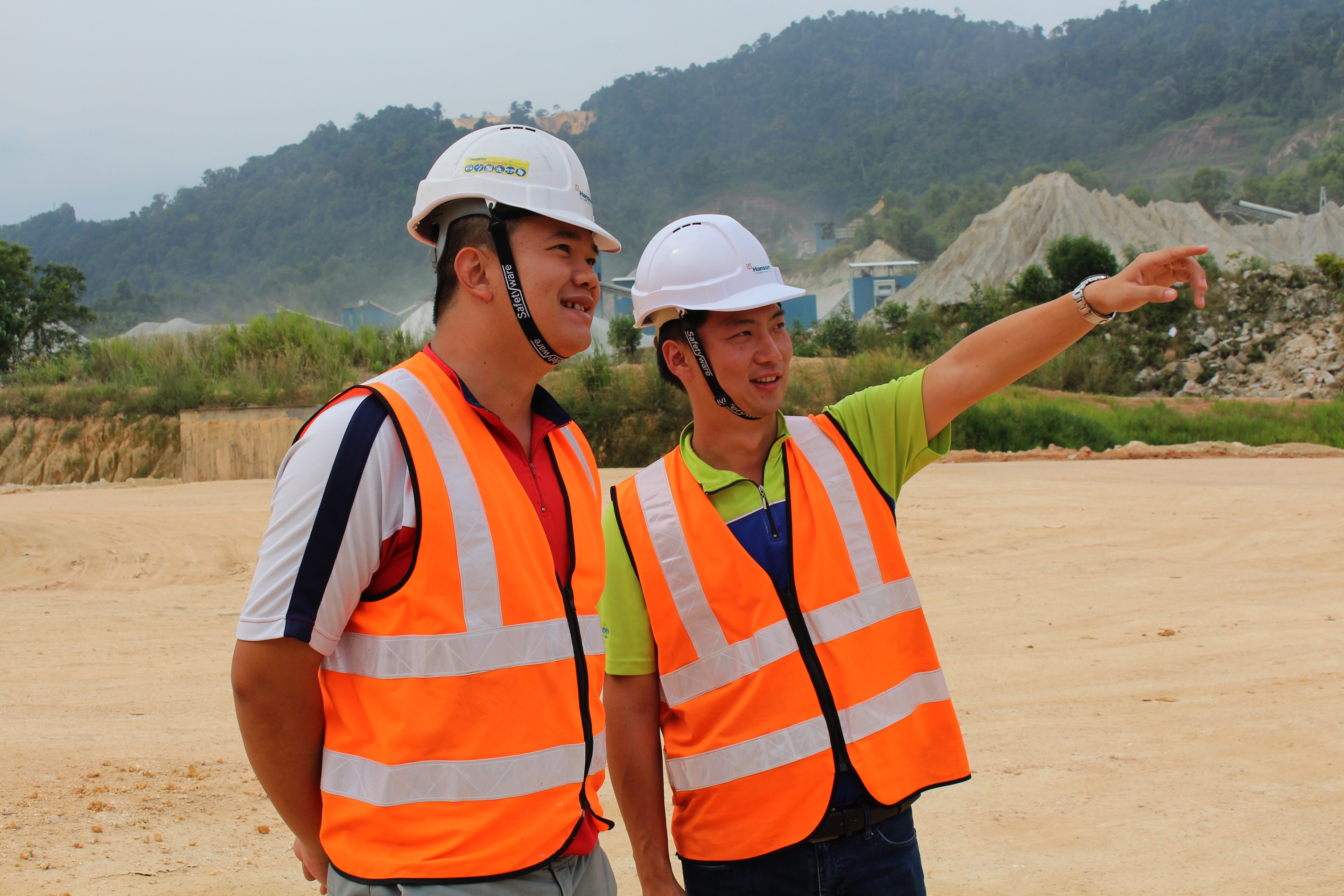 Two people with safety vests and hard hats on a quarry, one pointing into the distance