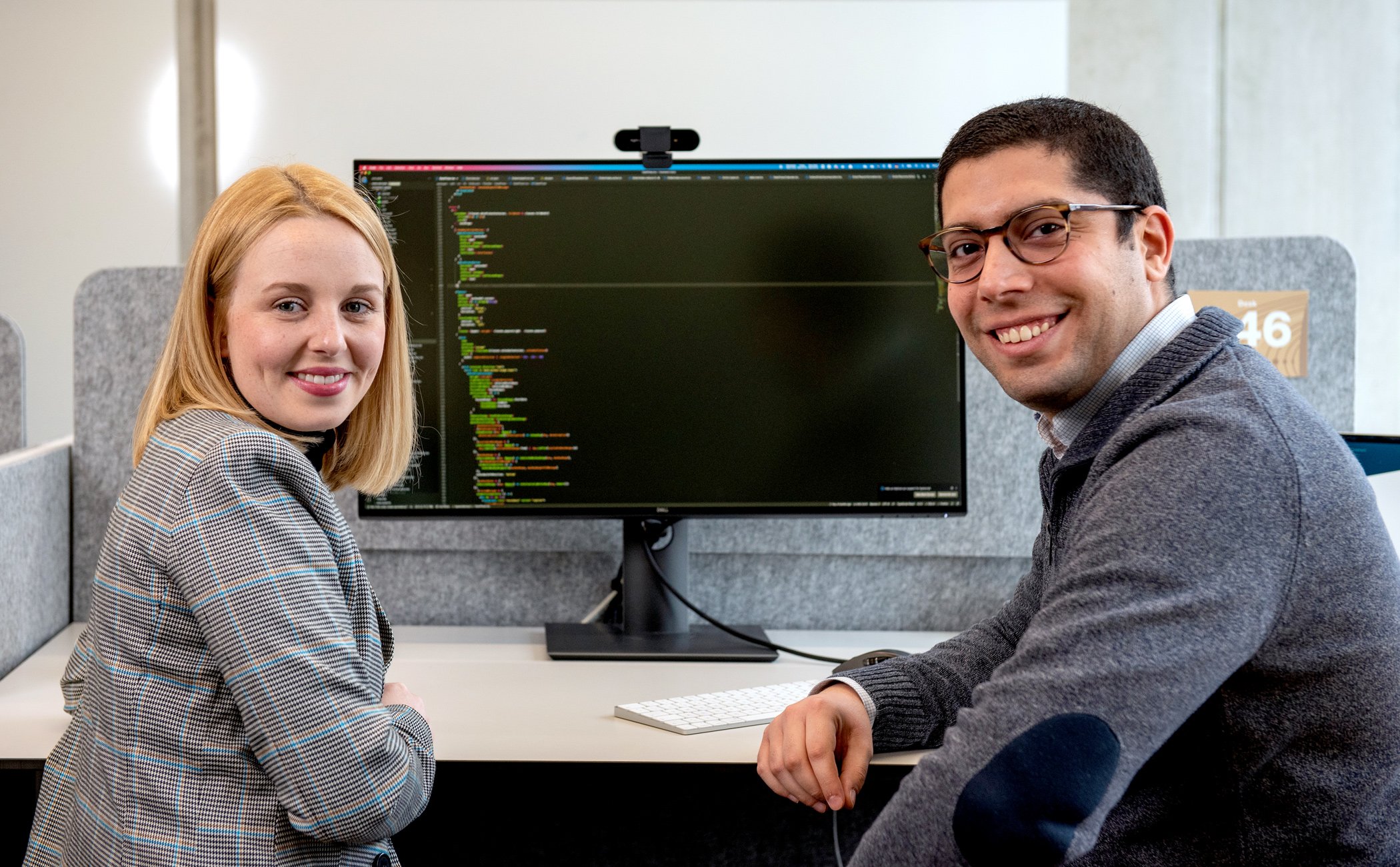 Zwei Kollegen sitzen vor einem Computer, auf dem Computer ist ein Code abgebildet
