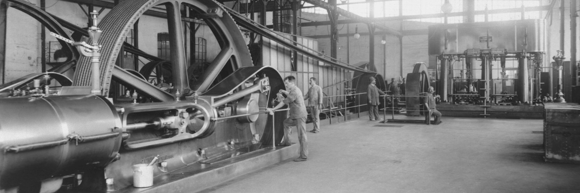 In einer Industriehalle arbeiten Arbeiter an einer Dampfmaschine