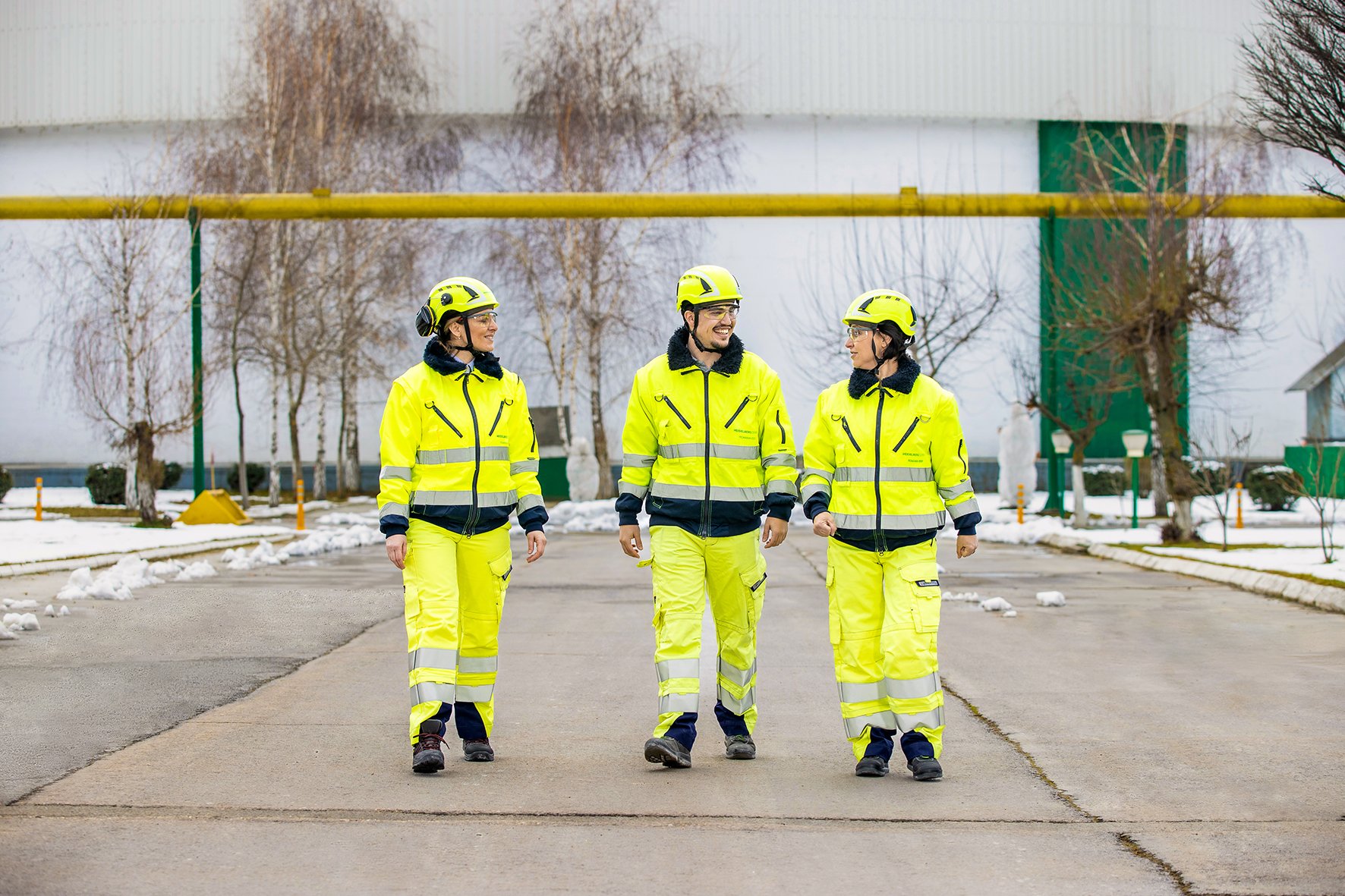 Three employees in yellow protective gear, two of them female, one male