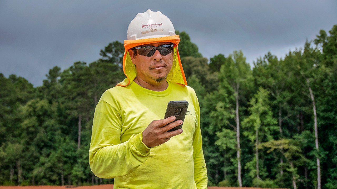 Ein Mann hält ein Mobiltelefon in der Hand, hinter ihm liegt ein Wald