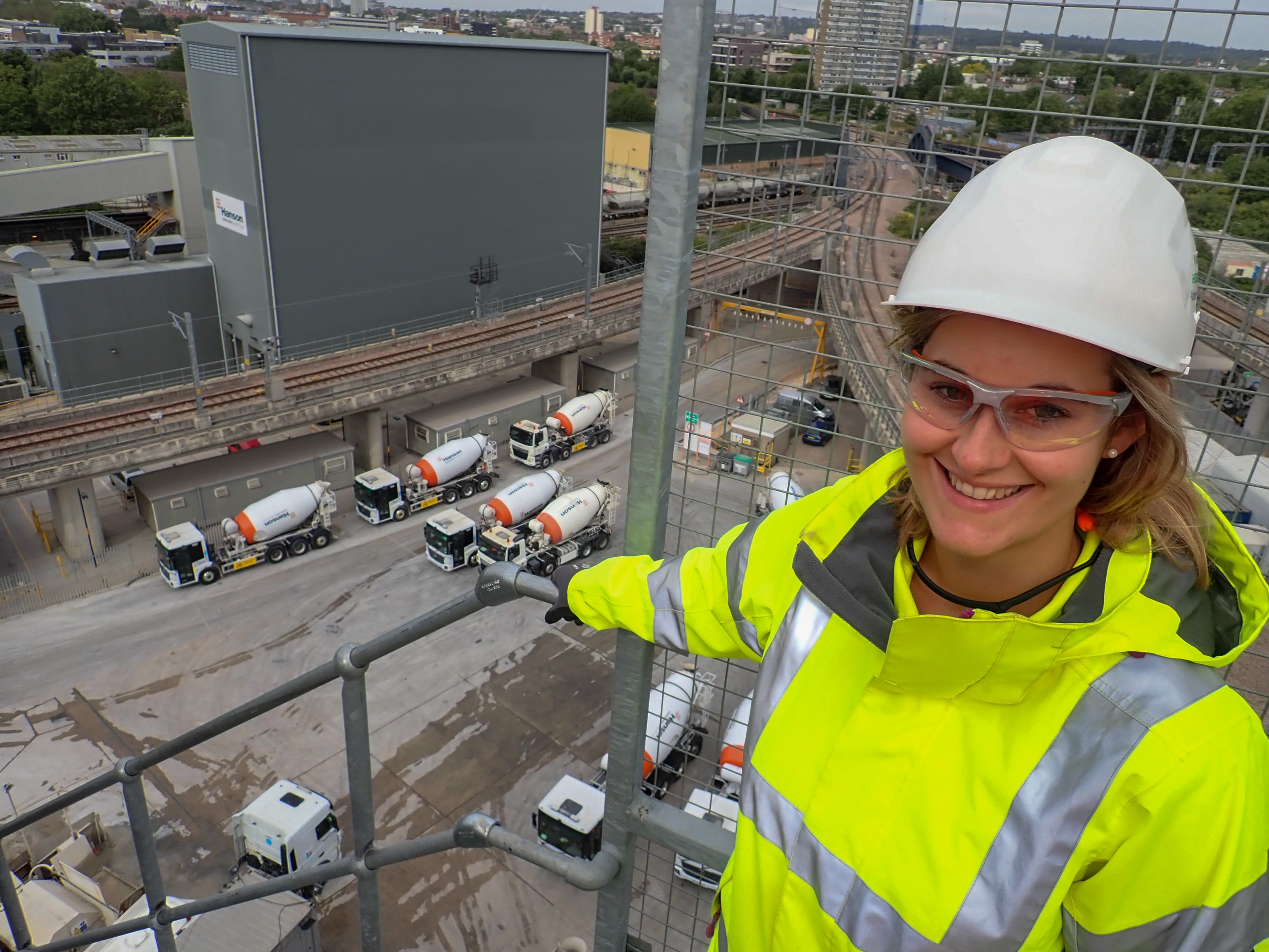Woman with construction helmet standing on an industrial plant, concrete mixer trucks below