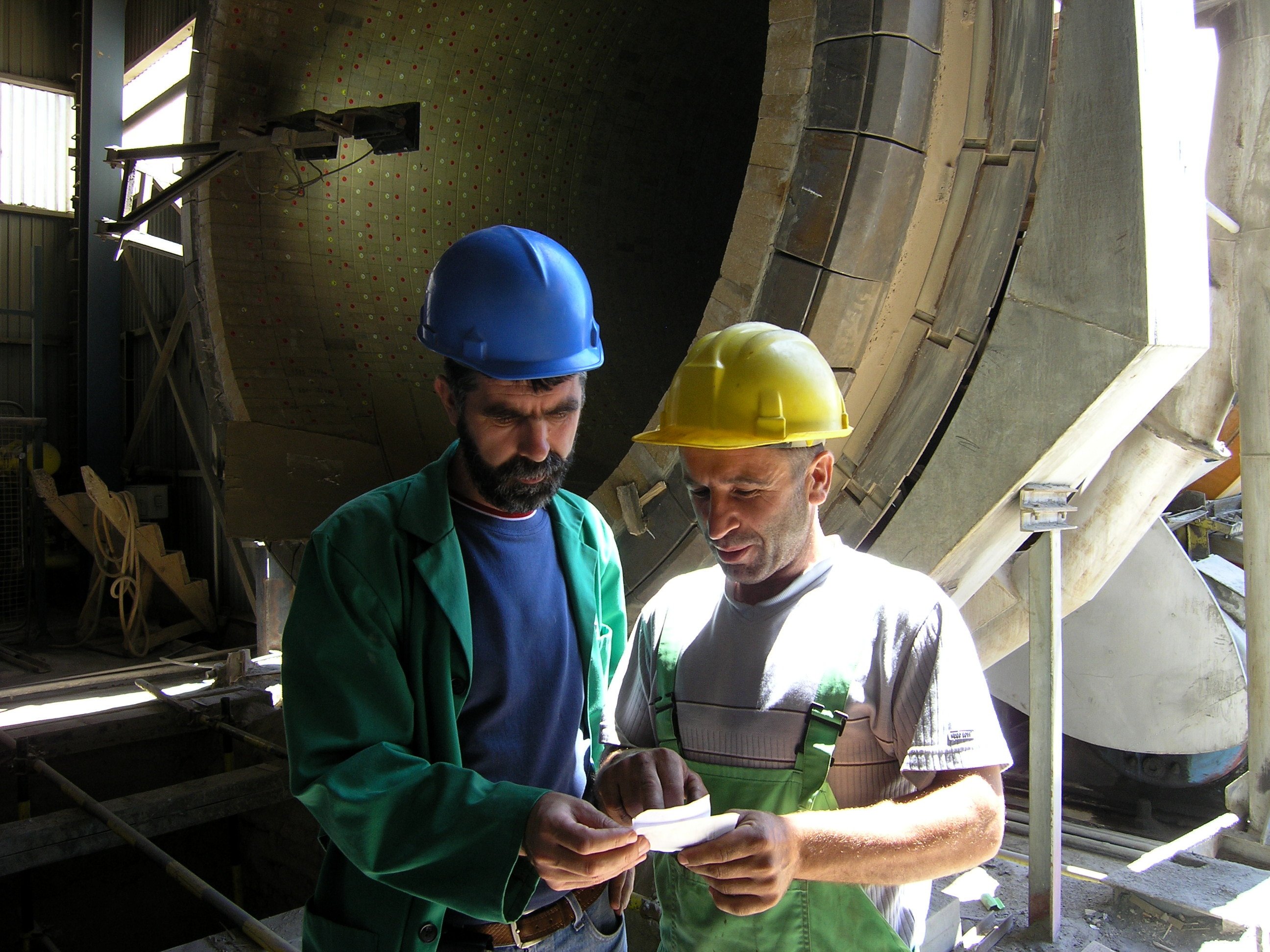 Two construction workers with helmets, both looking at a notebook
