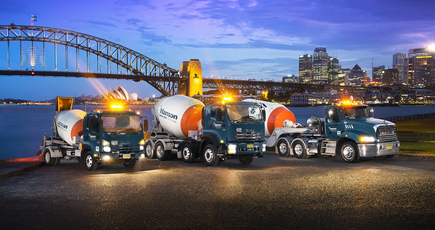 Three cement mixers with the inscription Hanson are standing on a bank, behind them is a skyline and a bridge with a round arch