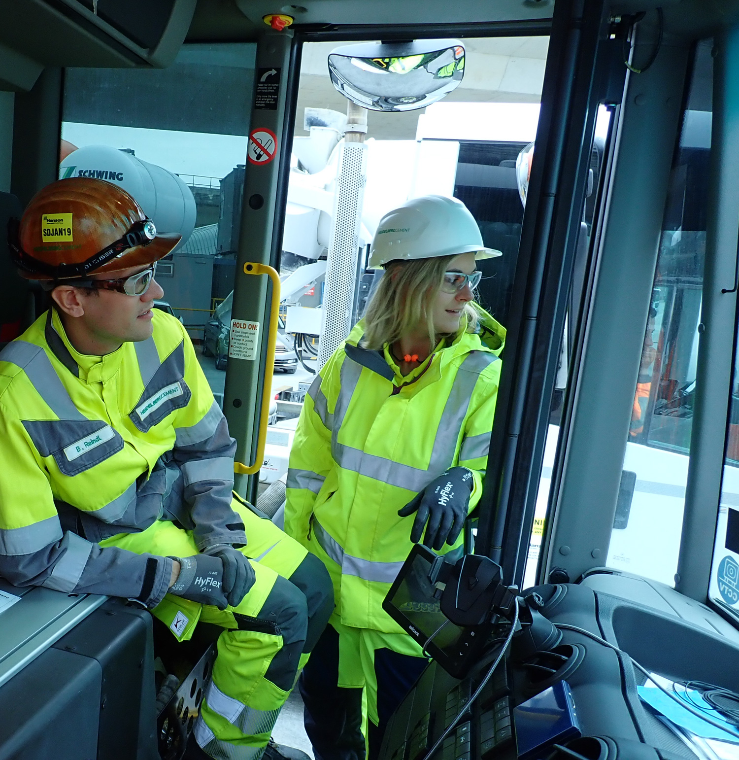 Man and woman in a truck, wearing hard hats and protective clothing